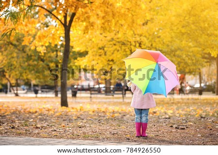 Little girl with rainbow umbrella in autumn park
