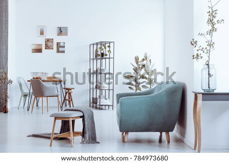 Blanket on bench and grey armchair in bright room with chairs at dining table against wall with gallery