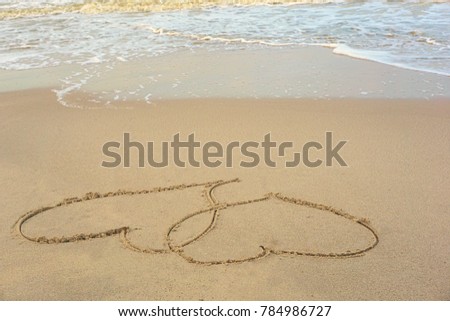 Two hearts overlapping images was written by hand on a beach by the sea. The picture represents our commitment and love of two people.