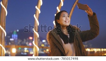 Asian woman taking photo on cellphone in the city of Hong Kong at night, bokeh city background 