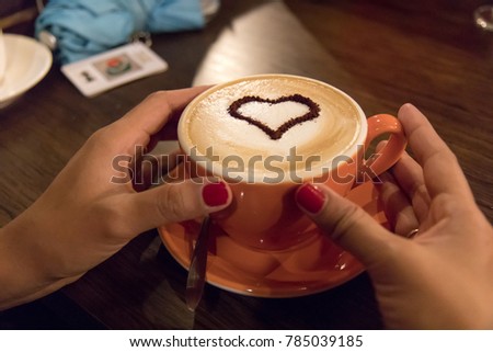 Female hand hold coffee cup with heart shape on wooden table.