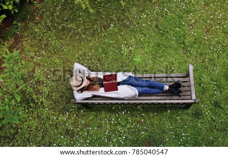 Girl with straw hat on a wooden bench with book. Italy