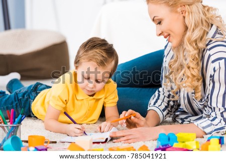young mother helping son while drawing picture together at home
