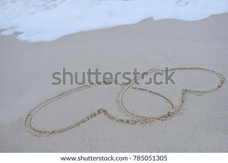Two hearts overlapping images was written by hand on a beach by the sea. The picture represents our commitment and love of two people.