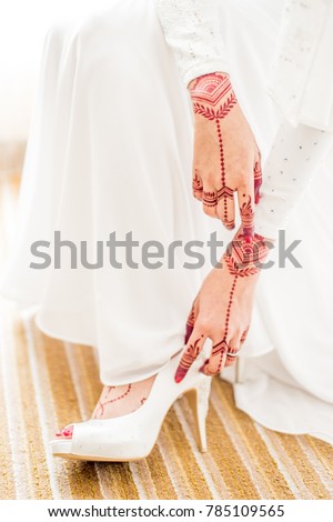 A beautiful bride wearing a beautiful white wedding shoe with henna on hand