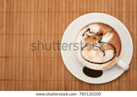 Cappuccino cup with cat drawn on a cream staying on bamboo table. 
