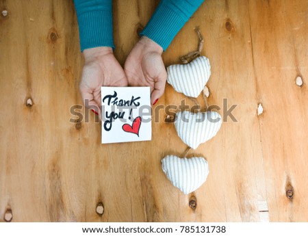 Woman's hands and note with Thank you text on rustic wooden table with three white hearts