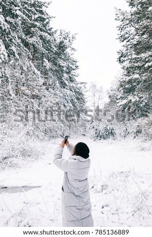 rear view of woman taking photo of snowy forest by smartphone