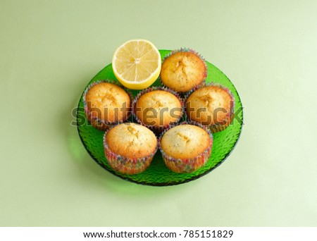 Lemon muffins with a piece of lemon on green glass plate on pale green background