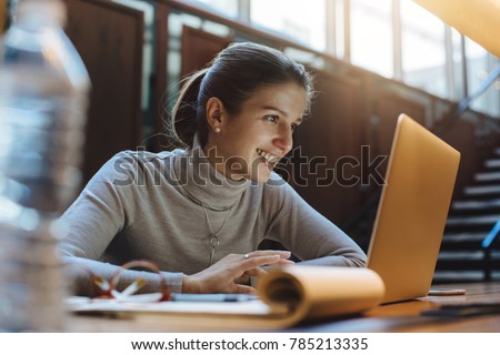 Happy smiling girl using laptop for studying in open work place