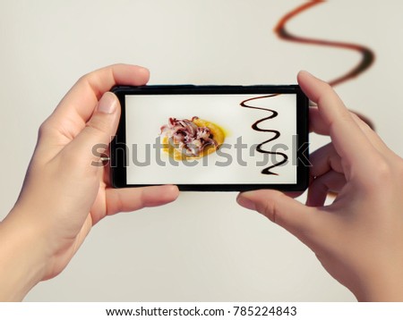 Female take picture of high quality food in a restaurant on white background on mobile phone. High quality cooking like octopus in yellow garlic sauce on smart phone. Luxury food isolated