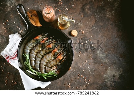 Raw fresh tiger shrimps with a cast-iron frying pan with fresh rosemary and pink salt. Healthy sea food. 