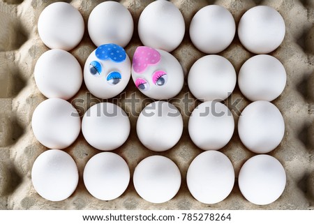Top view white eggs in cardboard container with Two funny eggs with love for each other. Unusual eggs with the beautiful eyes , cute muzzle.