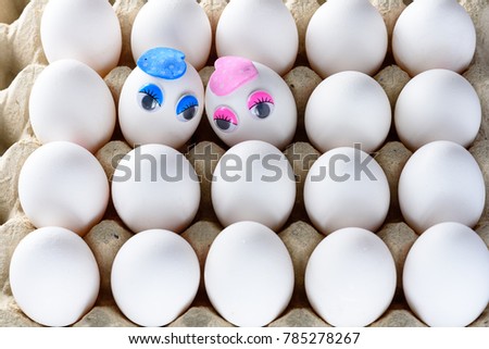Cute eggs with the face, eyes , muzzle. Two eggs with love for each other on chicken white eggs background in cardboard container.