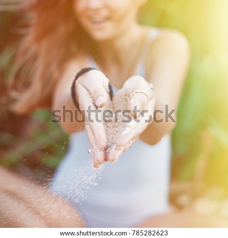 Cheerful woman sits in lotus pose and keeps sand in hands. Square picture