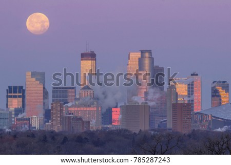 A Telephoto Close Up Compressing the Skyline of Minneapolis Reflecting the Sunrise as the Full Moon Sets Behind the City during the Morning Twilight