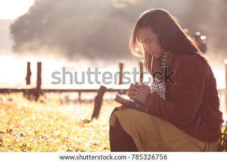 Woman hands folded in prayer on a Holy Bible for faith in beautiful nature background with sunlight in vintage color tone