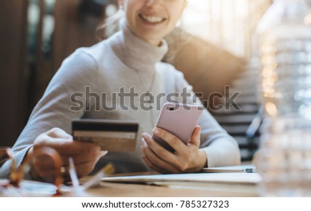Close-up young smiling girl holding credit card to pay online at internet shop while sitting at modern office