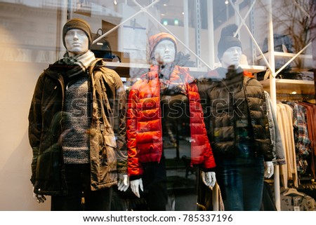 Men's and women's clothing store. Three mannequin dressed in parka, jackets, hat, behind the glass