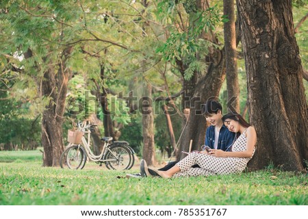 Asian couple lifestyle in park outdoor,reading book and listen to music for relaxation and happy in summer