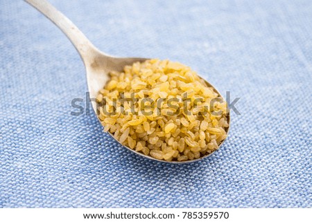 Bulgur grain in spoon on fabric background. Closeup view.
