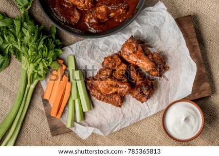 Buffalo chicken wings with cayenne pepper sauce served hot with celery sticks and carrot sticks cheese sauce.
