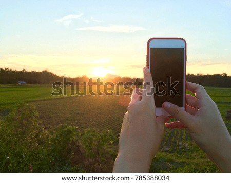Hand using phone taking photo beauty sunset and field farm