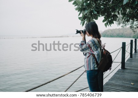 travel background beautiful photographer young women stand alone on wood bridge and hold camera take photo sea view. image for photography, person, portrait, scenery, lifestyle, nature concept