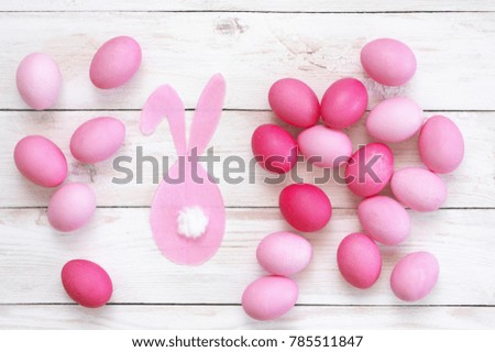 Varicolored pink Easter eggs with rabbit decor on rustic white wooden table. Top view point.