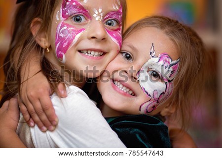Funny cute little girls with painting faces are hugging ang having fun. Royalty-Free Stock Photo #785547643