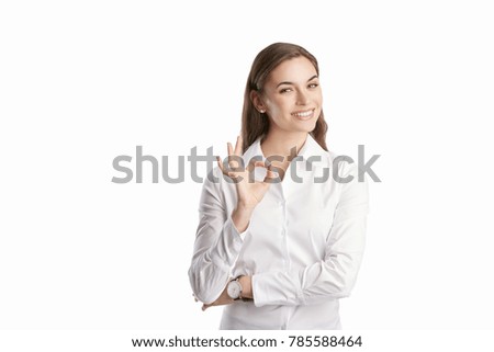 Beautiful young woman gesturing okay sign while standing at isolated white background. 