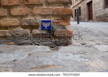 A blue pottery tile with a yellow menorah on it in a brick wall in the Jewish quarter of Toledo, Castile-La Mancha, Spain, a UNESCO World Heritage Site Royalty-Free Stock Photo #785595604