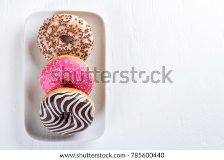 Three colorful donut on a plate on a white table. Selective focus.