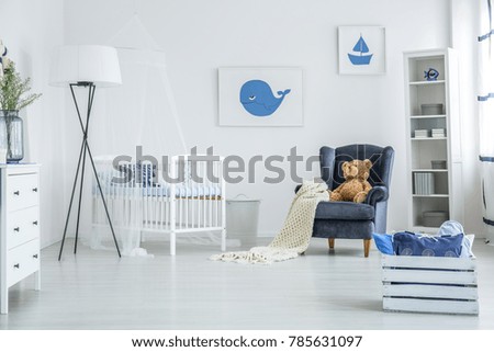 Pillows in wooden crate standing in front of blue armchair with teddy bear on it in bright kid's room