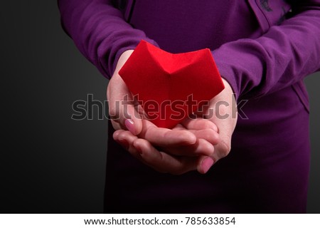 Girl in an ultra violet dress holding a Valentine's Day symbol in her hands. Red heart made of paper. Symbol of love. 