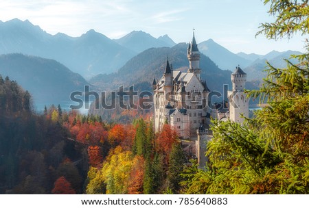 Neuschwanstein Castleon on Sunset with Mountain Hills on Background and colorful leafes, Amazing autumn Landscape. Picture of the fairy tale Castle near Munich in Bavaria, Germany. Postcard