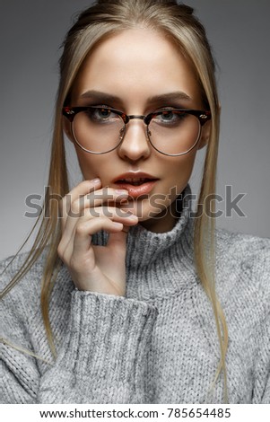 A young blonde girl with straight hair and gentle makeup. Beautiful model in a winter sweater and with glasses. Shining skin. Beauty of the face. Photo is taken in the studio. Cozy image
