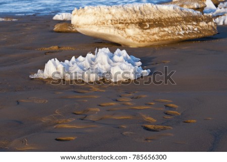 Ice and snow figure formation on beach sand near sea water and foot prints in bright sunny winter day