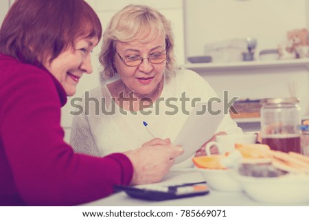 Smiling pensioners females at the table with utilities bills at home