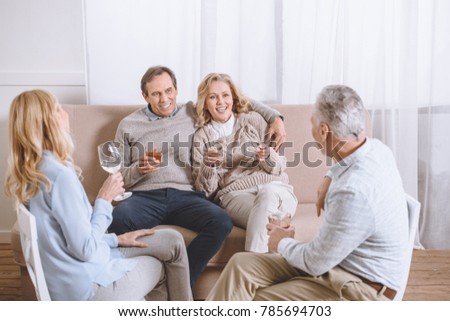 friends with glasses in hands speaking while sitting on sofa in room