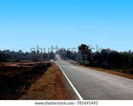 An Indian highway road with blue clear sky forest trees field towards horizon through rural landscape nice stock photo