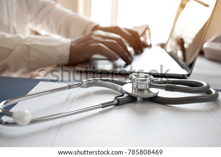Doctor's working on laptop computer, writing prescription clipboard with record information paper folders on desk in hospital or clinic, Healthcare and medical concept. Focus on stethoscope Royalty-Free Stock Photo #785808469