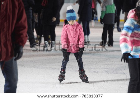 Child young girl ice skating at the ice rink outdoors. Child learning to skate on public rink.  Ice skaters using a temporary rink during the Christmas and New Year holiday period