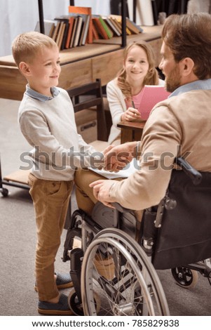 father on wheelchair and smiling son shaking hands