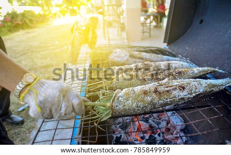 The snakehead is being roasted on a charcoal stove with a fire below it.