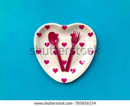 Closeup A pink heart printed paper plate with pink spoon,fork on pastel blue background.Invitation card for love party. 