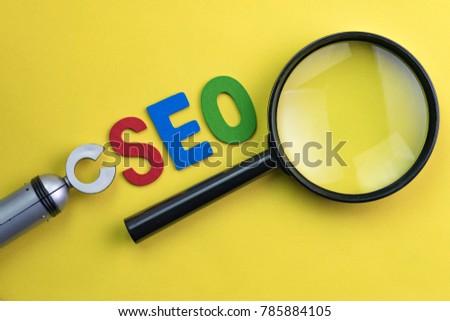 Magnifying glass, alphabet abbreviation SEO and robot arm on vivid yellow background using as SEO Search engine optimization concept.