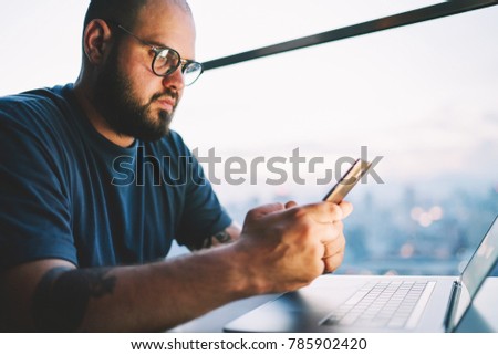 Cropped image of good looking confident freelancer in spectacles transferring money online and checking account balance via banking service.Bearded male person read news in website on telephone