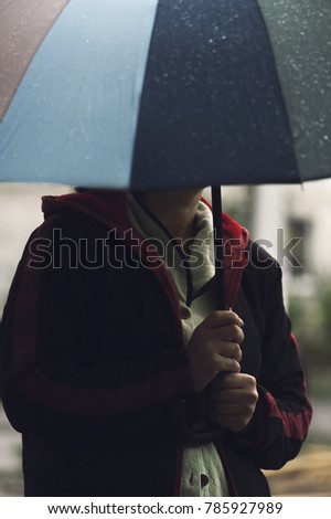 Man with colorful umbrella standing lonely and thinking in the rain weather, blur focus. Concept of loneliness and sadness