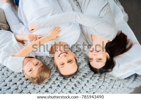 Full of affection. The top view of a happy young family lying on the bed, posing for the camera while smiling and hugging each other